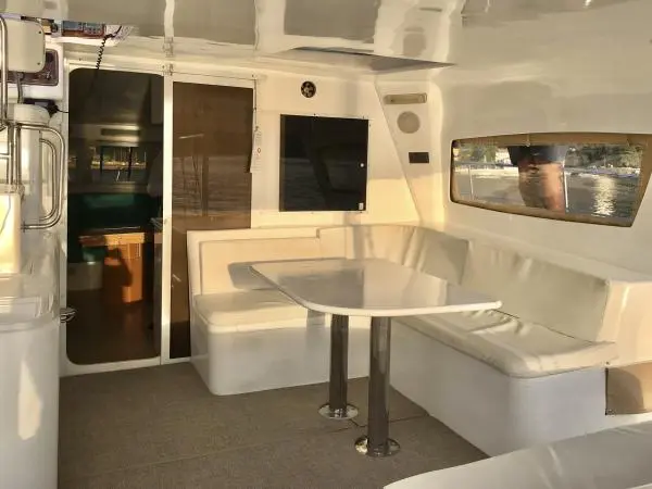 Área interna iluminada do Catamarã Power Cat 40 com assentos confortáveis e mesa, perfeita para lazer em passeios de barco.