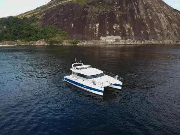Catamarã Power Cat 40 flutuando próximo a uma formação rochosa no Rio de Janeiro durante passeio privativo.