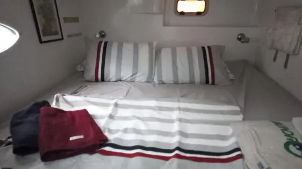 Quarto decorado no Catamarã Power Cat 40 com cama de casal, lençóis listrados e espaço confortável para pernoite.