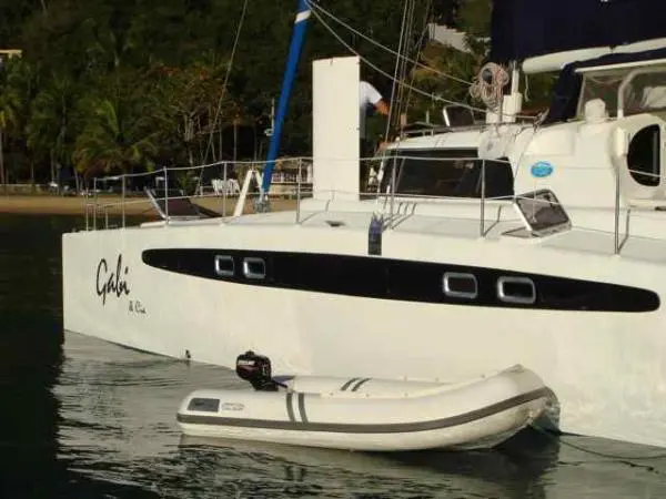 Lateral do Catamarã Dolphin 46 com bote inflável atracado ao lado, em águas calmas
