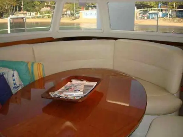 Área interna do Catamarã Dolphin 46 com sofá em formato de U e mesa central de madeira