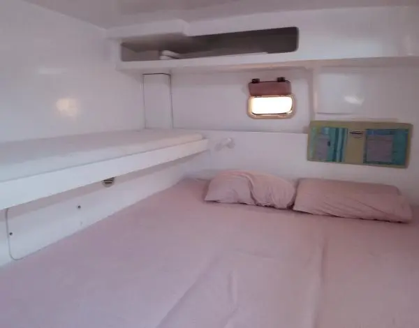 Cama de casal com lençóis claros em uma das suítes do Catamarã Power Cat 40, ideal para aluguel de barco com pernoite.
