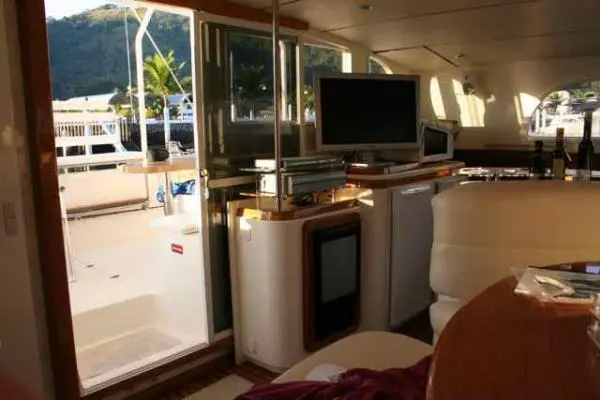 Vista da área interna do Catamarã Dolphin 46 para a área externa, com TV e equipamentos visíveis