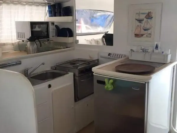 Cozinha equipada do Catamarã Power Cat 40, com geladeira, fogão e utensílios, ideal para conforto em passeios de barco.
