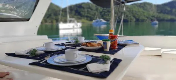 Mesa posta na área externa do Catamarã Power Cat 40 com vista para águas tranquilas e vegetação ao fundo.