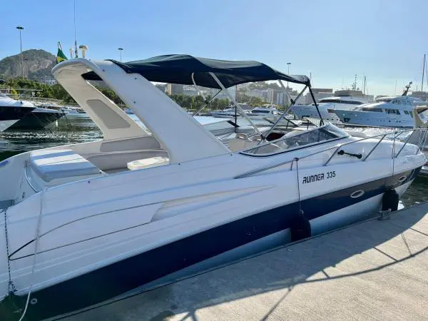 Lancha Runner 335 atracada em marina, com capota azul aberta e morro com bandeira do Brasil ao fundo
