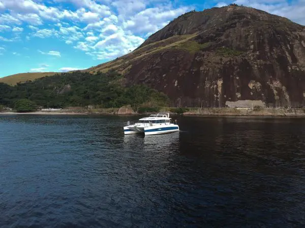 Catamarã Power Cat 40 navegando em águas calmas cercadas por montanhas no Rio de Janeiro, perfeito para aluguel de barco.