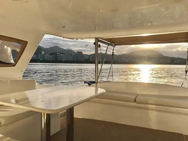 Área externa do Catamarã Power Cat 40 com vista para o pôr do sol em águas calmas do Rio de Janeiro.