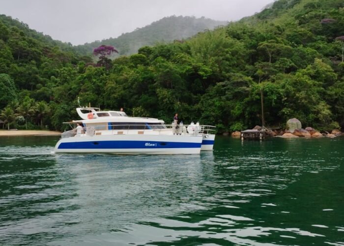 Catamarã Power Cat 40 navegando em águas tranquilas cercadas por vegetação exuberante no Rio de Janeiro. Ideal para aluguel de barco.