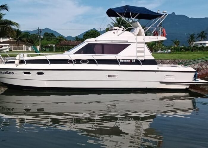 Lancha Intermarine Oceanic 32 com flybridge e toldo azul atracada em canal de marina, com montanhas ao fundo