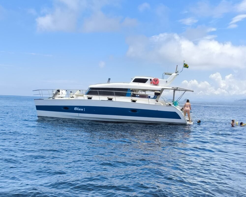 Catamarã Powercat 40 fundeado em mar aberto, com escada de popa em uso e pessoas nadando ao lado do casco