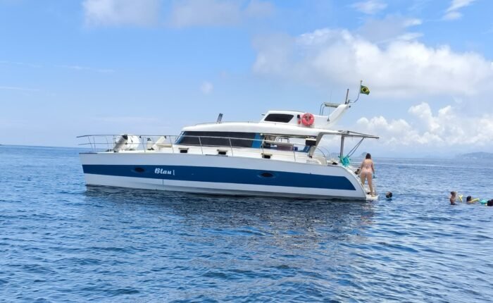 Catamarã Powercat 40 fundeado em mar aberto, com escada de popa em uso e pessoas nadando ao lado do casco