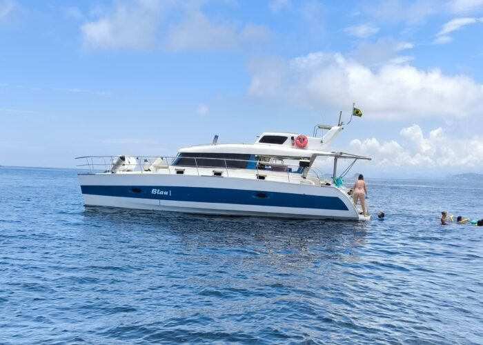 Catamarã Powercat 40 fundeado em mar aberto, com escada de popa em uso e pessoas nadando ao lado do casco