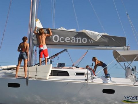Veleiro Wind 34 com tripulantes recolhendo a vela grande sobre a retranca, bimini aberto e boia salva-vidas na popa