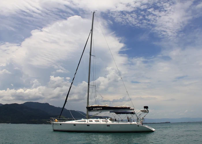 Veleiro One Off 47 fundeado em mar aberto, com mastro, bimini armado e costa montanhosa ao fundo