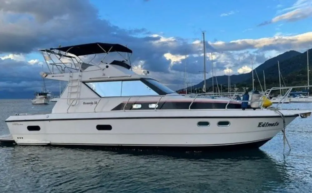 Vista lateral da lancha Oceanic 36 no mar, com montanhas ao fundo e céu parcialmente nublado.