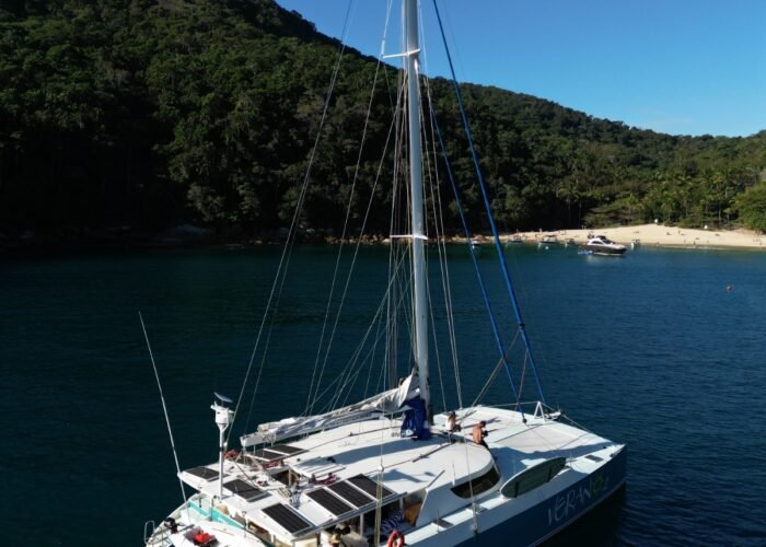 Vista aérea do catamarã 54 fundeado perto de praia, com painéis solares no convés e bote de apoio