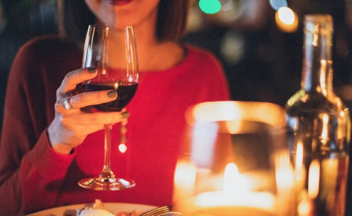 Mulher segurando uma taça de vinho em um ambiente iluminado por velas, criando uma atmosfera romântica e acolhedora.