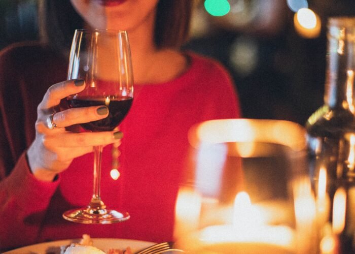 Mulher segurando uma taça de vinho em um ambiente iluminado por velas, criando uma atmosfera romântica e acolhedora.