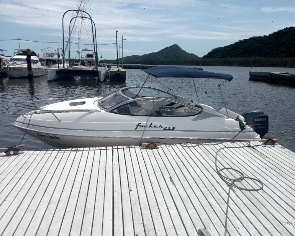 Vista lateral da lancha Focker 215 atracada em píer flutuante, com bimini armado, motor de popa e morros ao fundo