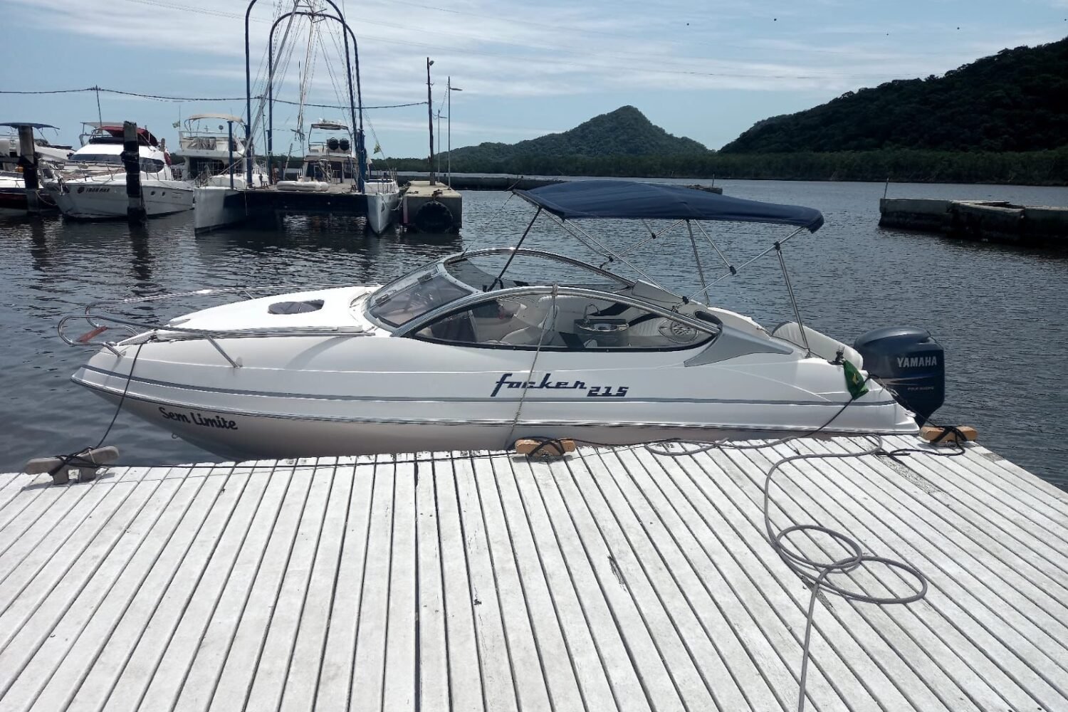 Vista lateral da lancha Focker 215 atracada em píer flutuante, com bimini armado, motor de popa e morros ao fundo