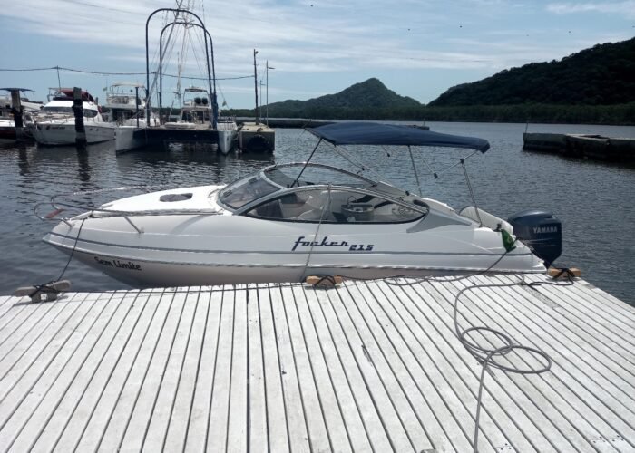 Vista lateral da lancha Focker 215 atracada em píer flutuante, com bimini armado, motor de popa e morros ao fundo