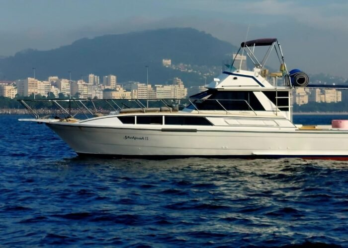 Lancha Carbrasmar 39 fundeada com flybridge e bimini, diante de prédios e morro na orla