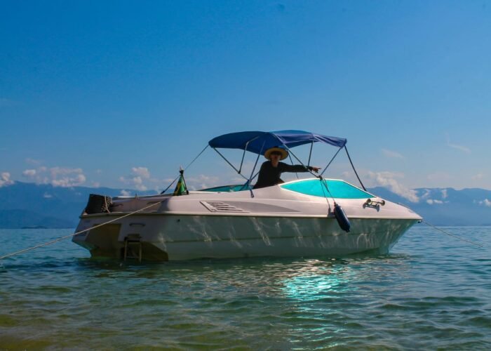 Lancha Ventura Open 23 fundeada em água rasa e clara, de perfil, com toldo bimini aberto e cabos de fundeio