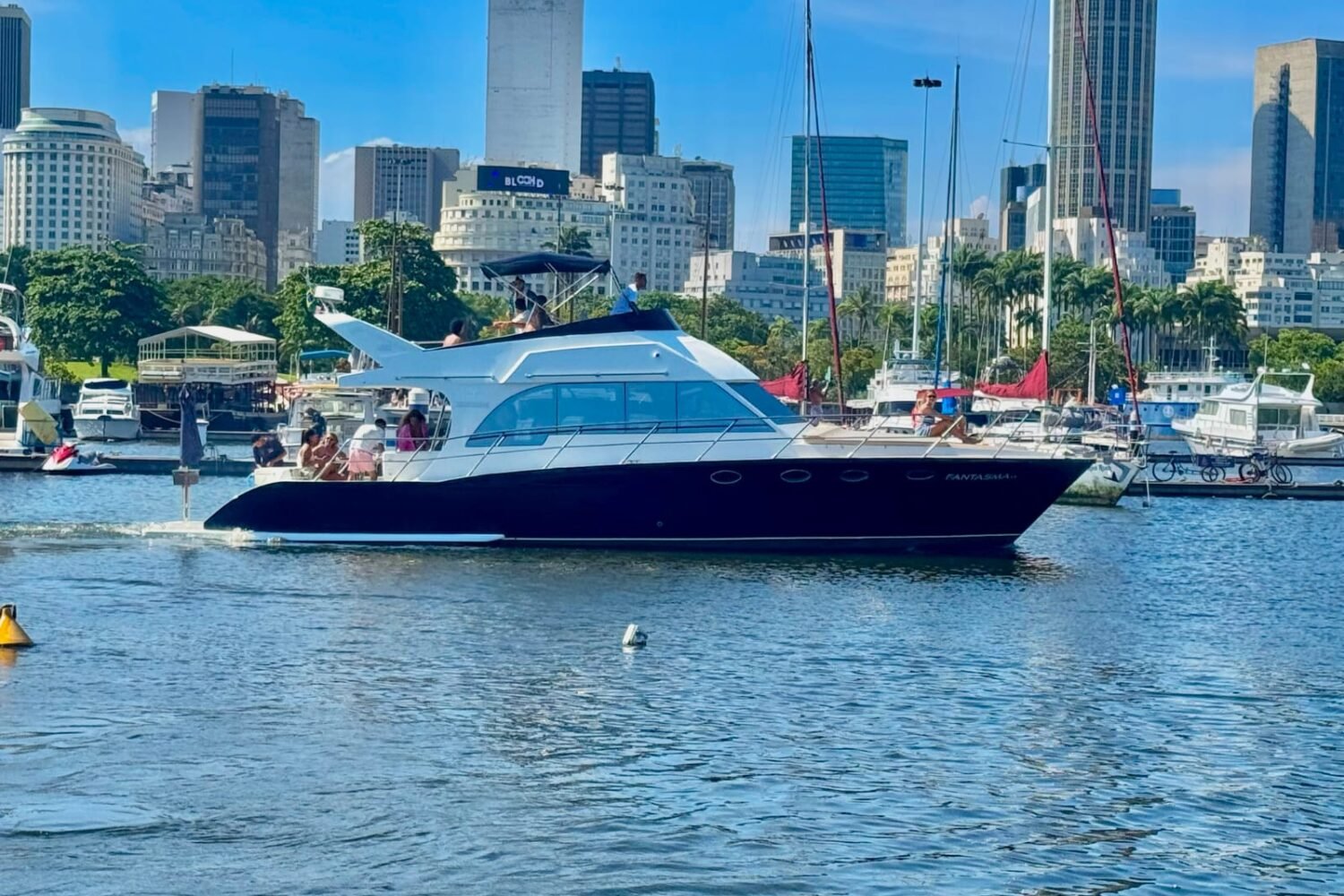 Lancha Tecnomarine 50 navegando com flybridge e toldo azul, com prédios do Rio de Janeiro ao fundo