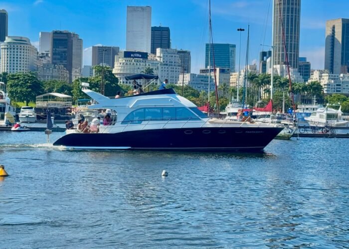 Lancha Tecnomarine 50 navegando com flybridge e toldo azul, com prédios do Rio de Janeiro ao fundo
