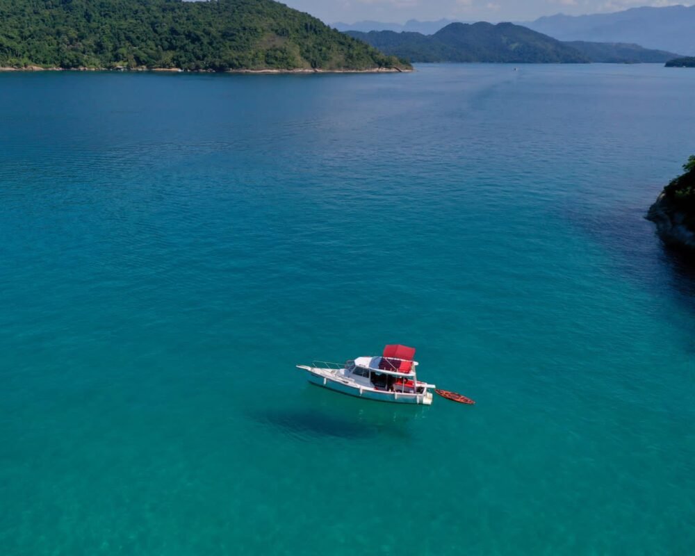 Barco traineira navegando em águas azuis com uma ilha ao fundo em Paraty.