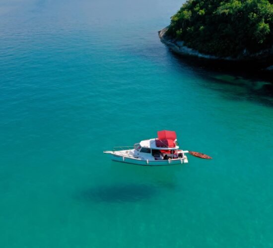 Barco traineira ancorado em águas cristalinas de Paraty, com um stand-up paddle ao lado.