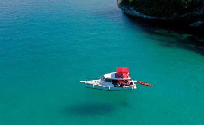 Barco traineira ancorado em águas cristalinas de Paraty, com um stand-up paddle ao lado.