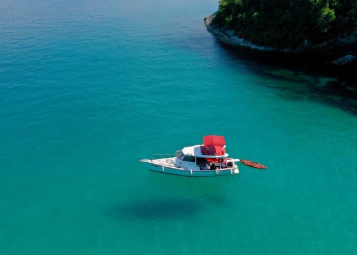 Barco traineira ancorado em águas cristalinas de Paraty, com um stand-up paddle ao lado.