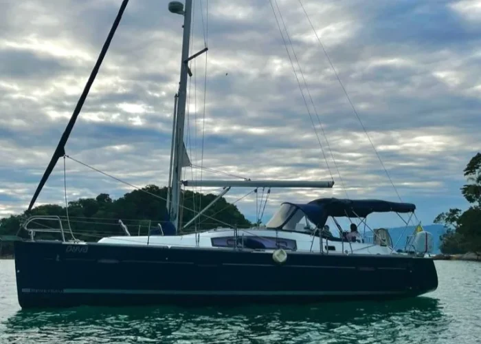 Veleiro Beneteau 40 de casco azul fundeado em mar calmo sob céu nublado, com bimini armado