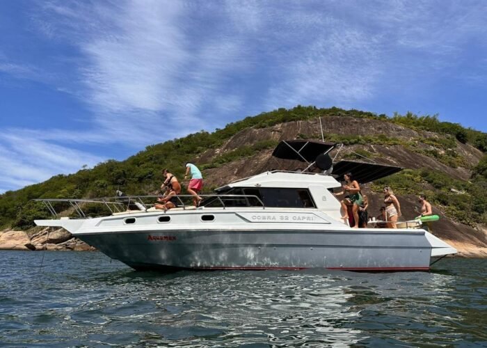 Lancha Cobra Capri 32 fundeada junto a costão rochoso com vegetação, com grupo a bordo