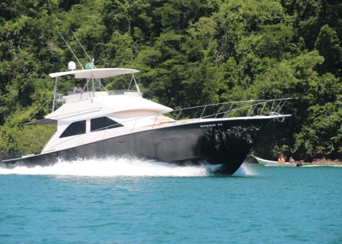 Lancha Ocean Pro 55 navegando com flybridge em mar verde-água junto à costeira com mata em Angra dos Reis