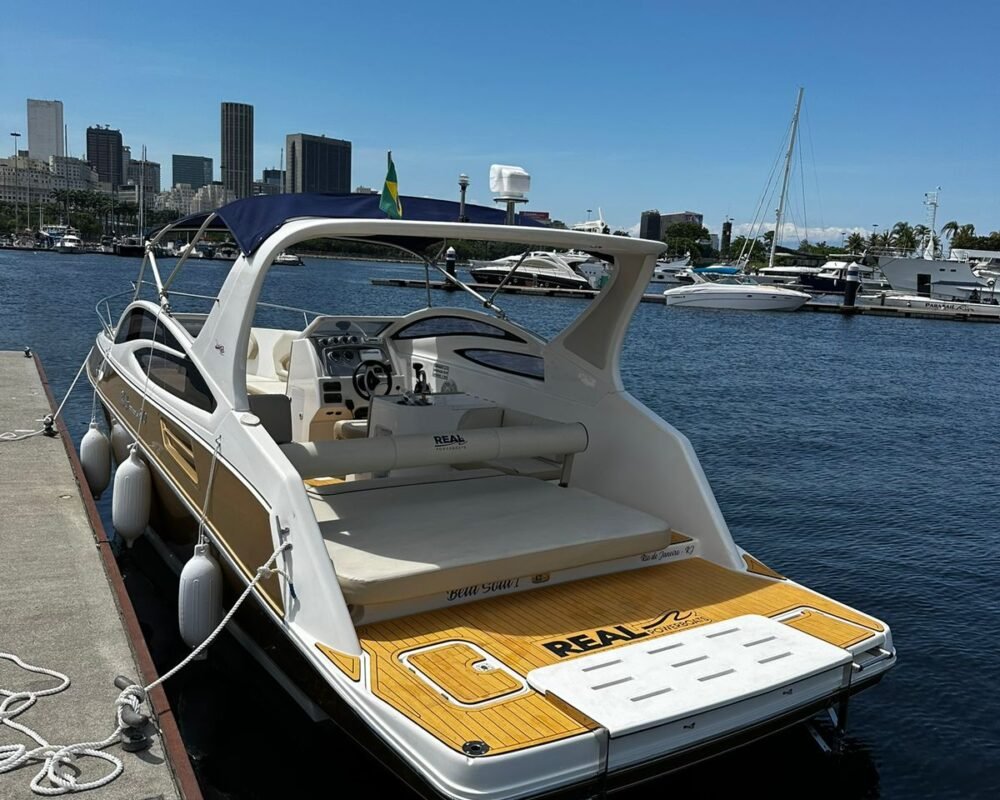 Lancha Real 270 ancorada na marina, com bandeira do Brasil e skyline do Rio de Janeiro ao fundo.