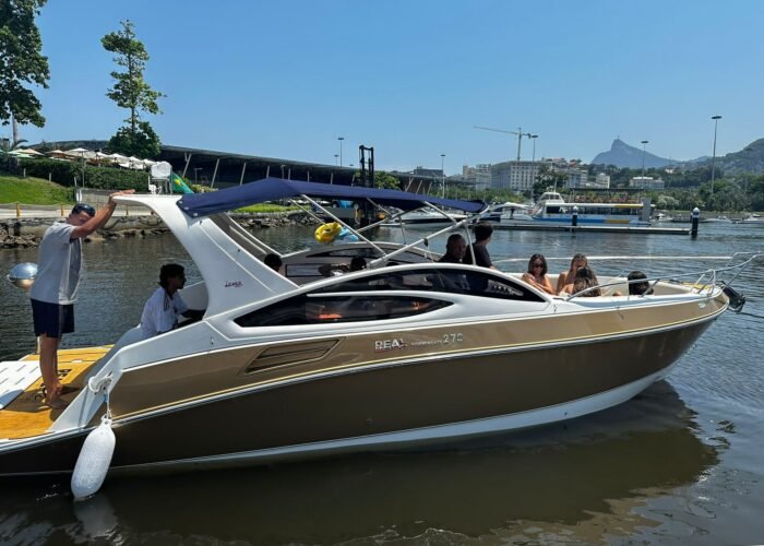 Lancha com passageiros aproveitando um passeio sob um céu azul, com o Cristo Redentor ao fundo.