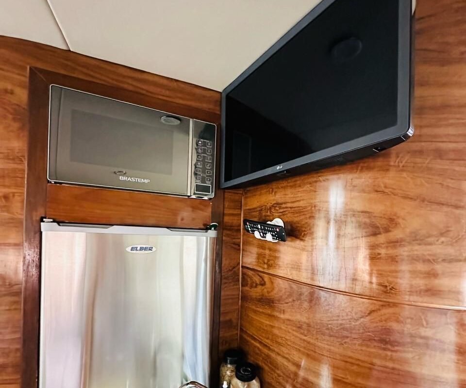 Pequena cozinha da embarcação equipada com micro-ondas, TV, geladeira e pia, ideal para armazenar alimentos e bebidas.