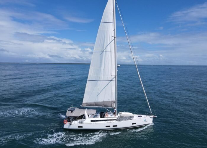 Veleiro Beneteau Oceanis 55 navegando com velas brancas içadas em mar aberto, com dois tripulantes no convés