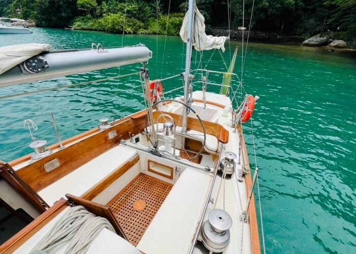 Cockpit de veleiro Columbia 50 com timão, estrado de teca e winches, fundeado em água turquesa