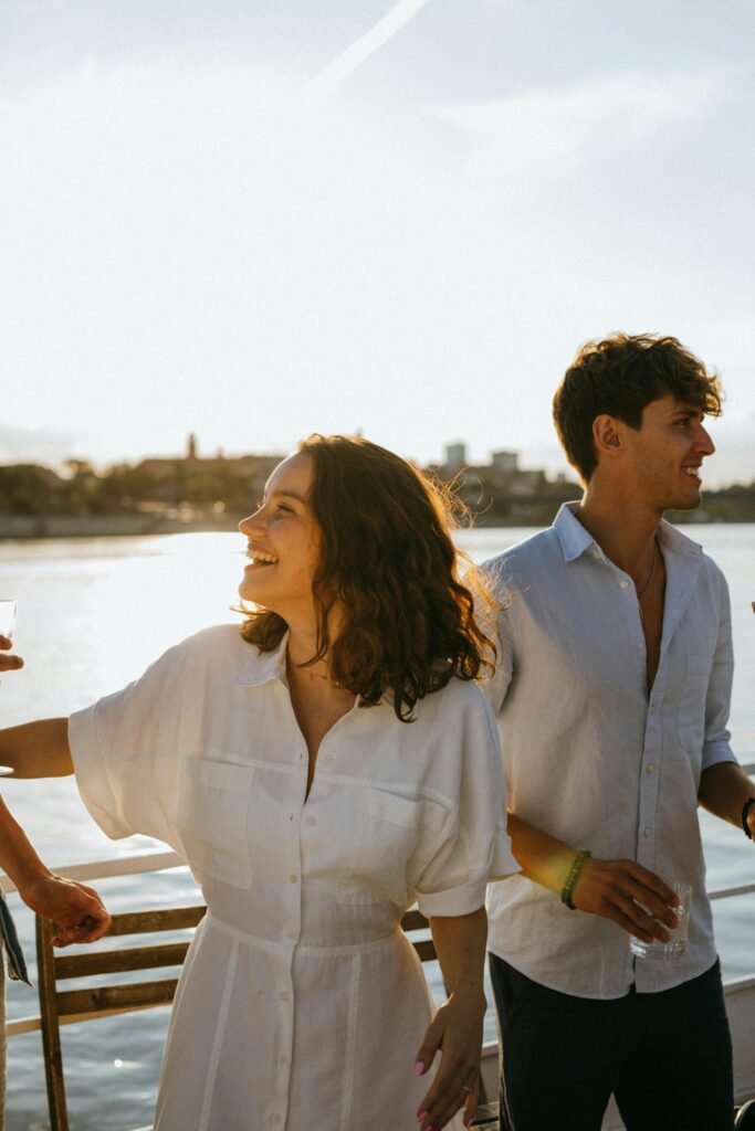 Casal em barco ao entardecer — mulher com vestido branco de linho e homem com camisa branca aberta