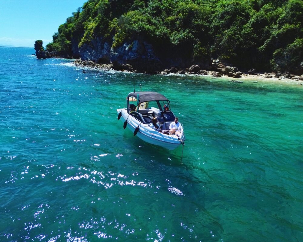 Lancha Coral 24 ancorada em uma enseada de águas cristalinas em Búzios, proporcionando um passeio relaxante com vista para a costa.