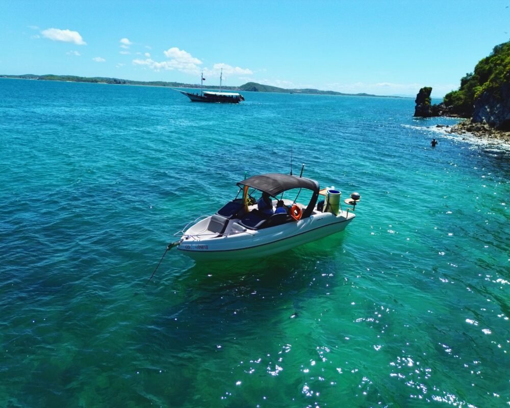 Lancha Coral 24 ancorada próxima a uma praia paradisíaca, com mar azul-turquesa e vegetação exuberante ao fundo.