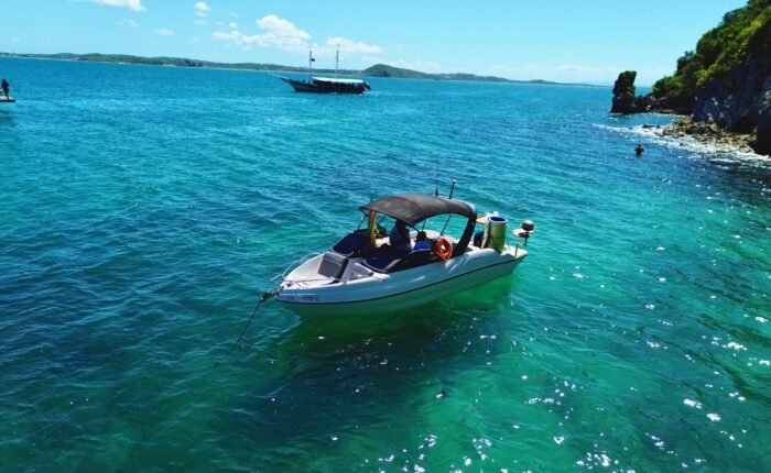 Lancha Coral 24 ancorada próxima a uma praia paradisíaca, com mar azul-turquesa e vegetação exuberante ao fundo.