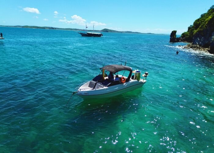 Lancha Coral 24 ancorada próxima a uma praia paradisíaca, com mar azul-turquesa e vegetação exuberante ao fundo.