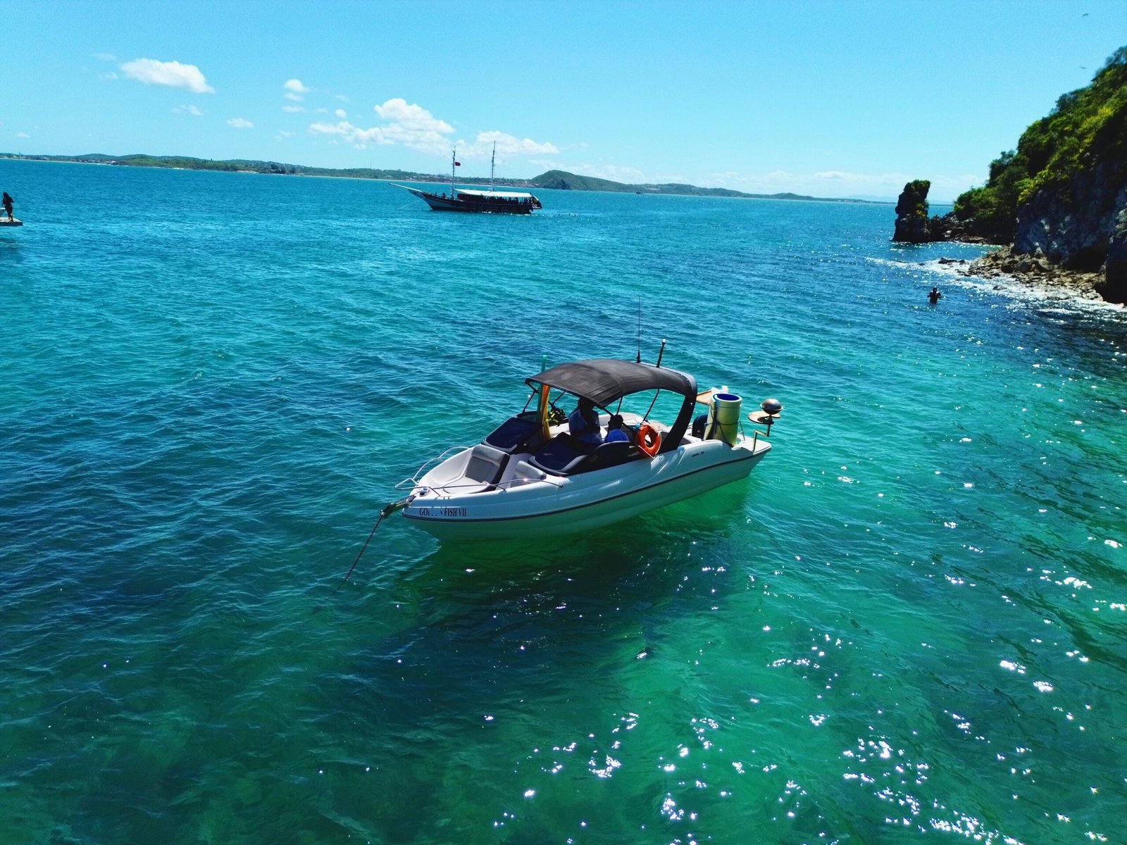 Lancha Coral 24 ancorada próxima a uma praia paradisíaca, com mar azul-turquesa e vegetação exuberante ao fundo.