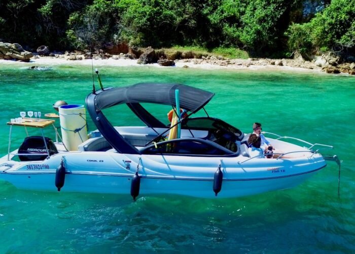 Vista lateral de lancha Coral 23 ancorada em enseada de águas turquesa com costão verde em Búzios