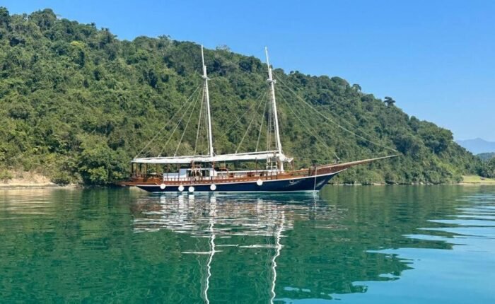 Escuna clássica navegando em águas cristalinas de Paraty, cercada por vegetação tropical.